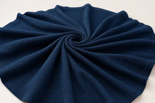 A dark navy blue textured fabric, likely a waffle-knit blanket or throw, arranged in a spiral pattern on a plain white background.