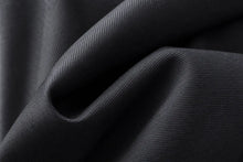 A close-up of draped black fabric with a fine ribbed texture, showing soft folds and shadows.