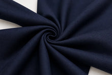 A close-up of dark navy blue fabric arranged in a spiral swirl, showing the material texture and color against a small white background.