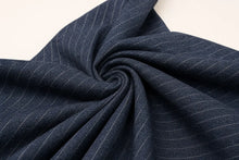 A close-up of dark navy blue fabric with thin white pinstripes, arranged in a spiral drape against a light off-white background.