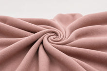 A close-up of dusty pink fabric arranged in a spiral swirl, showing its soft texture and drape against a light neutral background.