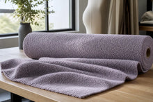 A rolled and draped light purple textured fleece blanket on a wooden table in a modern room setting.