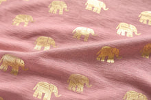 A close-up of dusty pink fabric with a repeating pattern of metallic gold and cream elephant silhouettes.