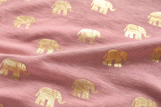 A close-up of dusty pink fabric with a repeating pattern of metallic gold and cream elephant silhouettes.