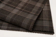 Dark brown and black plaid fabric with fine gray stripes, folded to show the texture and scalloped edges on a white background.