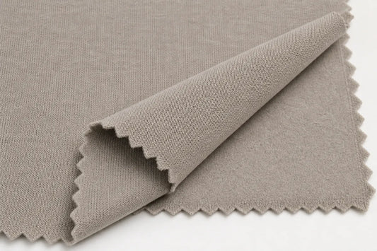 A close-up of a light taupe gray woven fabric with scalloped edges, folded over to show its texture against a plain white background.