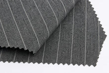 Dark gray pinstriped fabric with fine white vertical stripes, folded to show texture and scalloped cut edges on a white background.