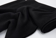 A close-up of a black textured knit fabric, shown draped with a rolled section on a plain white background.