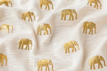 White textured fabric with a repeating pattern of small metallic gold elephants, shown in soft folds.