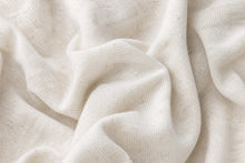 A close-up of draped off-white knit fabric with a soft, textured weave and gentle folds.