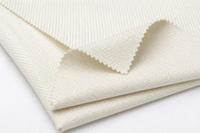 A close-up of folded cream-colored fabric with a textured, woven surface and a serrated cut edge, shown on a plain white background.