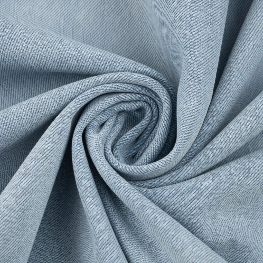 A close-up of light blue-gray fabric arranged in a spiral swirl, showing the material texture and drape.