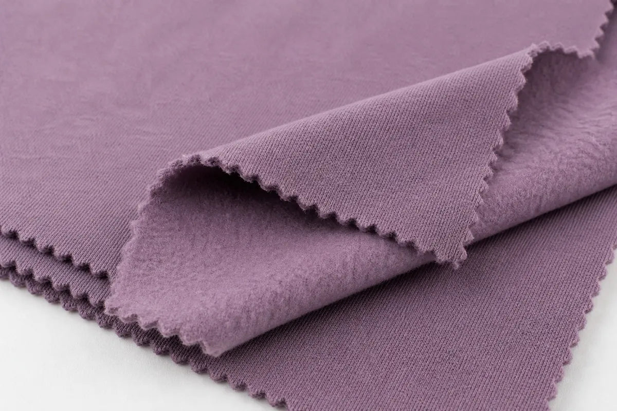 A close-up of a folded dusty purple fabric with scalloped edges, showing its texture and color against a white background.