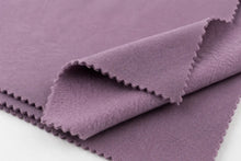 A close-up of a folded dusty purple fabric with scalloped edges, showing its texture and color against a white background.