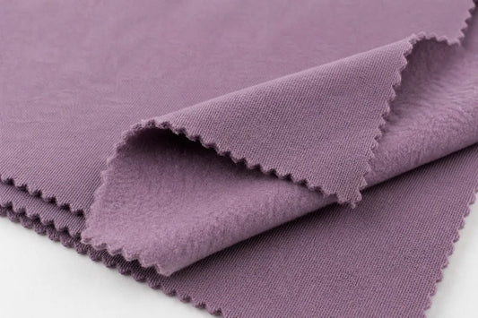 A close-up of a folded dusty purple fabric with scalloped edges, showing its texture and color against a white background.