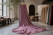 A dusty mauve-pink fabric drape hanging from a black clothing rack in a bright, modern textile studio with other fabric swatches visible in the background.
