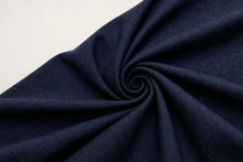 A close-up of dark navy blue textured fabric arranged in a spiral swirl on a light off-white background.