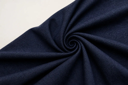 A close-up of dark navy blue textured fabric arranged in a spiral swirl on a light off-white background.