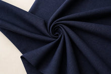 A close-up of dark navy blue fabric arranged in a spiral drape against a light off-white background.