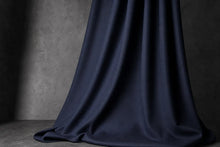 A draped piece of dark navy blue satin fabric cascading down against a textured gray studio background.