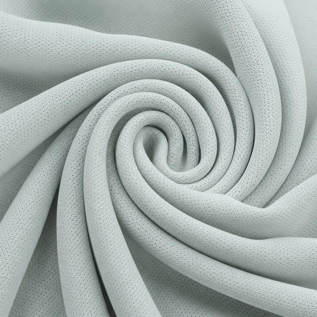 A close-up of light gray textured fabric arranged in a spiral drape, showing a fine mesh-like surface.