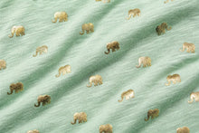 A close-up of a sage green fabric with a repeating pattern of small metallic gold elephants.
