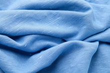 A close-up of light blue textured fabric with soft folds and a woven slub pattern.