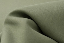 A close-up of draped olive green fabric with a fine ribbed texture, showing soft folds and shadows.