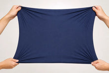 A navy blue fabric sheet is stretched horizontally by four hands against a plain light gray background.
