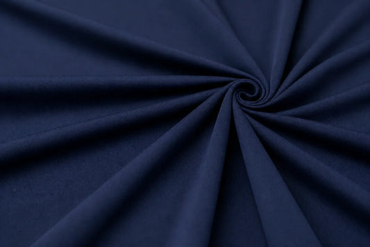 A close-up of dark navy blue fabric arranged in a spiral drape pattern, showing the material texture and color.