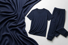 A navy blue two-piece loungewear set consisting of a short-sleeve crewneck t-shirt and matching drawstring pants, styled flat-lay on a light gray background with a draped navy fabric prop.