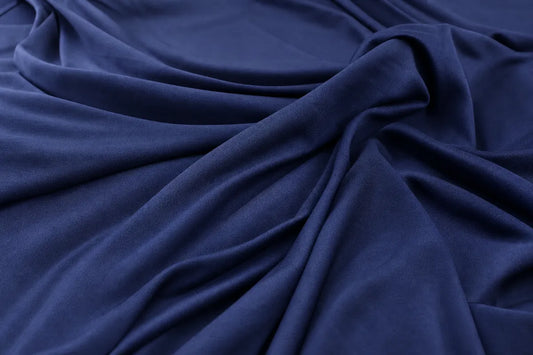 A close-up of draped navy blue fabric with soft folds and a smooth texture.