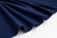 A close-up of dark navy blue fabric draped in soft folds over a plain white surface.