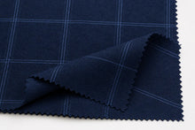 A close-up of dark navy blue fabric with a fine light blue windowpane plaid pattern, folded over on a white background.