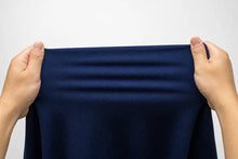A pair of hands holding up a dark navy blue textured fabric against a plain light gray background.