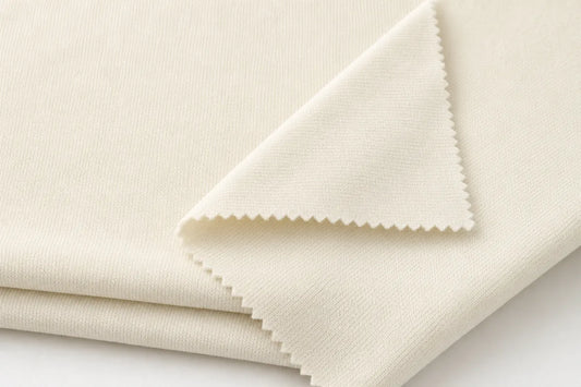 A close-up of folded cream-colored fabric with a visible woven texture and zigzag-cut edges, photographed on a clean white background.