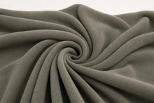A close-up of draped fabric in a muted taupe-gray color, arranged in a spiral fold pattern against a plain light background.