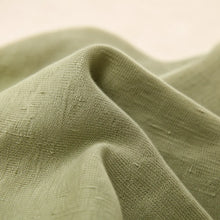 A close-up of draped olive green woven fabric with a soft, textured surface and a light cream background.