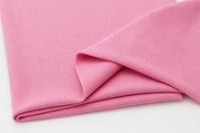 A close-up of folded pink ribbed fabric, likely jersey or knit material, shown on a plain white background.