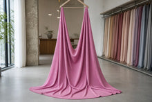A draped pink fabric or dress hanging from a wooden hanger in a bright, modern fabric showroom with other color swatches visible in the background.