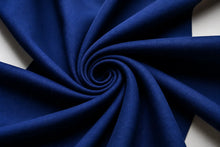 A close-up of deep blue fabric arranged in a spiral swirl, showing the material texture and drape against a light neutral background.