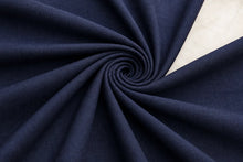A close-up of dark navy blue fabric arranged in a spiral drape, with a small section of light beige fabric visible in the upper right corner.
