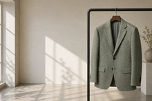 A light sage green textured blazer jacket hanging on a black clothing rack in a minimalist room with warm sunlight and window shadows.