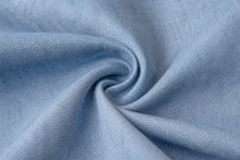 A close-up of light blue textured fabric arranged in a spiral swirl, showing the weave and material detail.