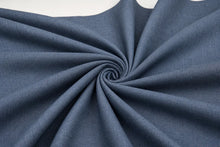 A close-up of slate blue fabric arranged in a spiral drape, showing its fine woven texture against a white background.