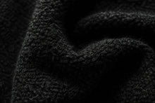 Close-up of a black textured knit fabric with soft folds and a ribbed pattern.