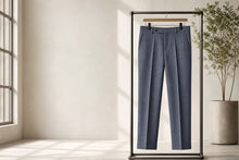 A pair of blue pinstriped trousers hanging on a wooden hanger inside a black clothing rack, set in a minimalist room with a window and a potted plant.