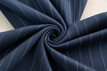 A close-up of dark navy blue fabric with thin white pinstripes, arranged in a spiral drape on a light neutral background.