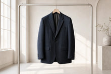 A dark navy blue pinstripe blazer hangs on a wooden hanger from a minimalist metal clothing rack in a bright, modern room with soft natural light.