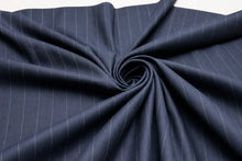 A close-up of dark navy blue fabric with thin white pinstripes, arranged in a spiral drape pattern against a white background.